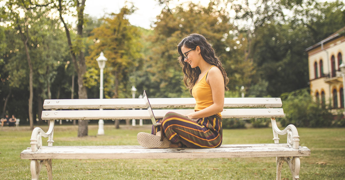 A woman on her laptop sitting on a park bench