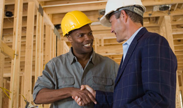 Two men in hard hats shaking hands on construction site